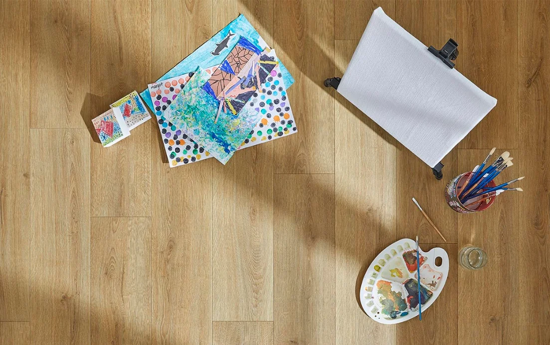 Light wood-look floors with a child’s art supplies show how durable laminate flooring is.